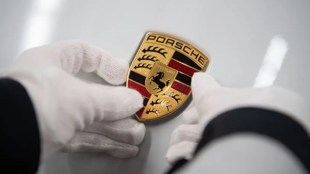 ARCHIV - 04.03.2020, Baden-Württemberg, Stuttgart: Eine Mitarbeiterin der Porsche AG hält in der Produktion ein Porsche-Emblem auf die Motorhaube eines Porsche Taycan. (zu dpa: «Porsche lässt Produktion weitere Woche ruhen") Foto: Marijan Murat/dpa +++ dpa-Bildfunk +++