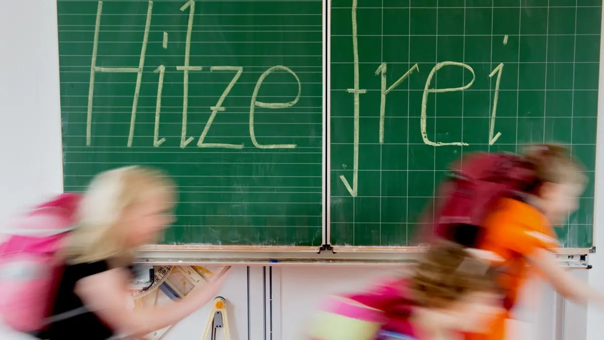 ILLUSTRATION - Schüler einer 2. Klasse laufen in einer Grundschule an einer Tafel mit der Aufschrift "Hitzefrei" vorbei. Wer Hitzefrei hat, kann schnell nach hause oder ins Freibad.