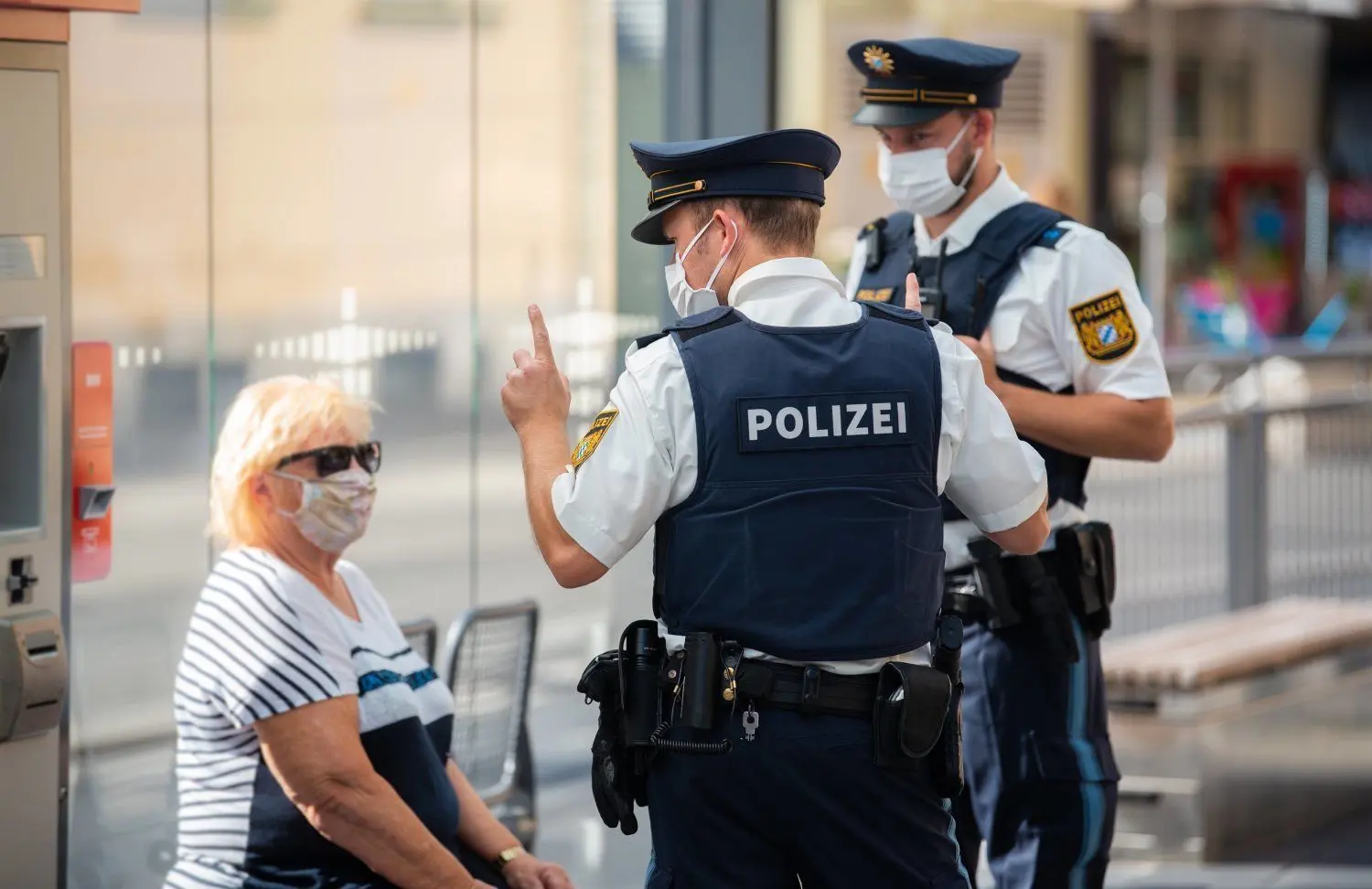 Zwei Polizisten nehmen an einer Tram-Haltestellenach einem Verstoß gegen die Maskenpflicht im öffentlichen Nahverkehr die Personalien einer Frau auf.