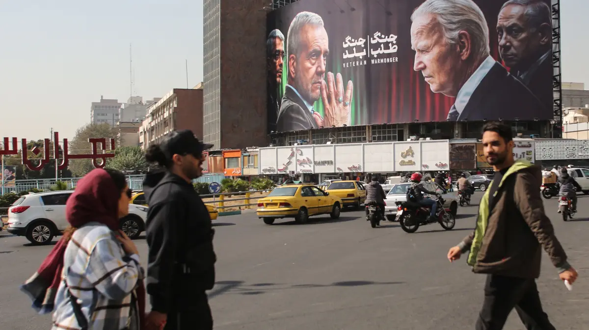 People walk past a billboard bearing pictures of Iran's President Masoud Pezeshkian (2-L), armed forces chief of staff Major General Mohammad Bagheri (L) US President Joe Biden (2-R) and Israeli Prime Minister Benjamin Netanyahu (R) in Vali-Asr square in Tehran on October 27, 2024. On October 26, Israel carried out air strikes against military sites in Iran in response to Tehran's missile attack on October 1, itself a retaliation for the killing of Iran-backed militant leaders and a Revolutionary Guards commander. (Photo by ATTA KENARE / AFP)
