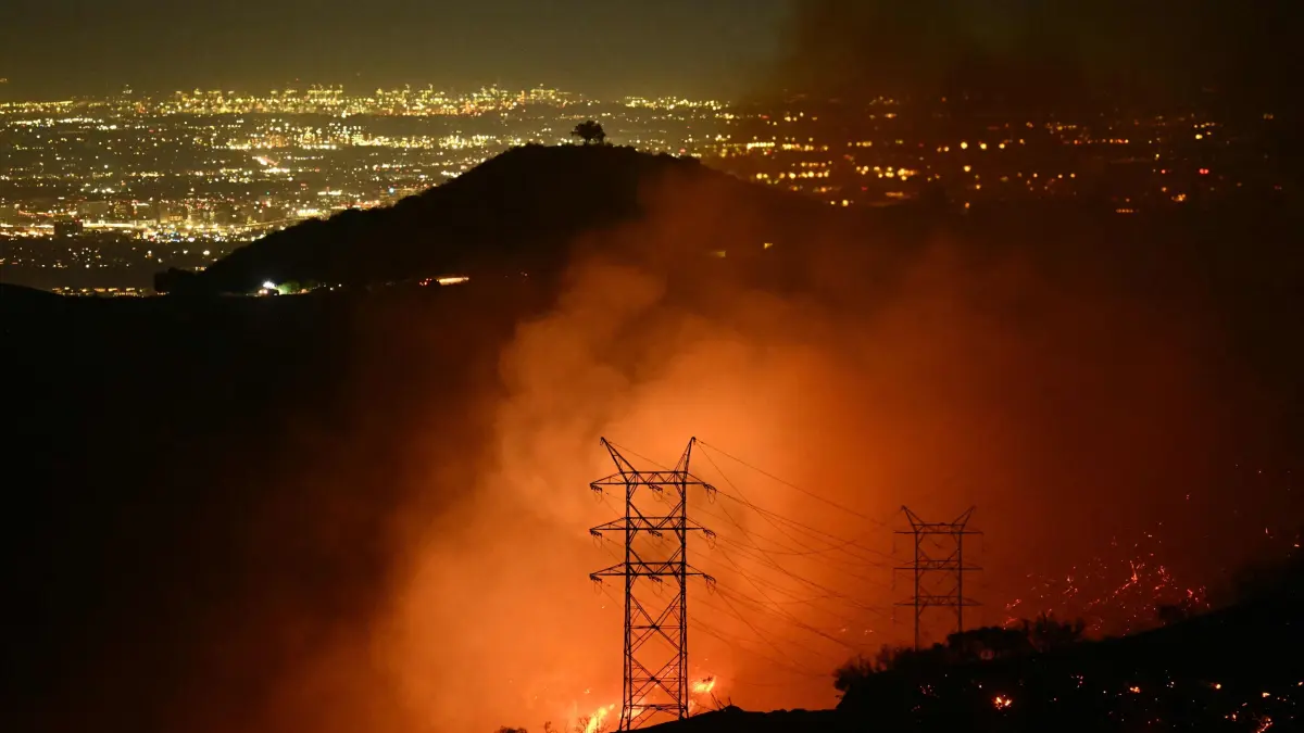 Flames and smoke are seen near power lines as the Palisades fire grows near the Mandeville Canyon neighborhood and Encino, California, on January 11, 2025. The Palisades Fire, the largest of the Los Angeles fires, spread toward previously untouched neighborhoods January 11, forcing new evacuations and dimming hopes that the disaster was coming under control. Across the city, at least 16 people have died as multiple fires have ripped through residential areas since January 7, razing thousands of homes in destruction that US President Joe Biden likened to a "war scene." (Photo by Patrick T. Fallon / AFP)