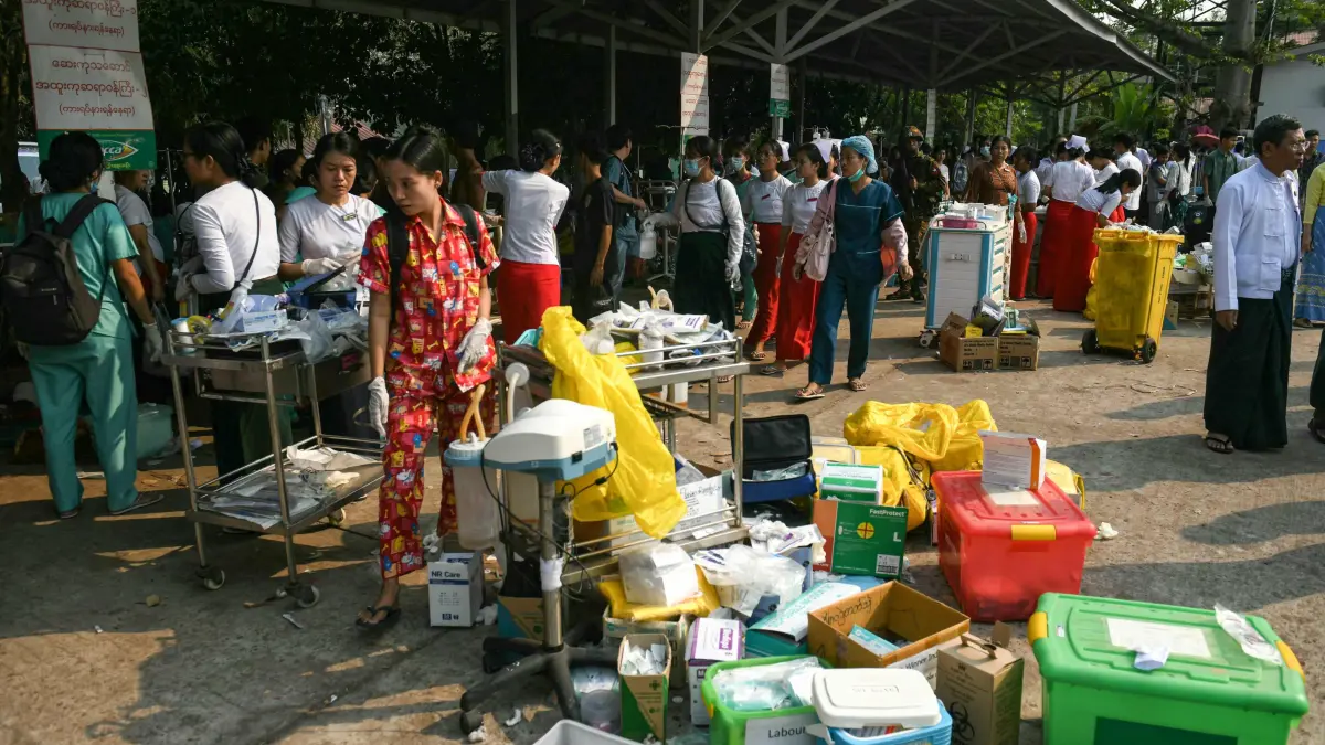 Medical workers and people walk past boxes of medical material placed in the compound of a hospital in Naypyidaw on March 28, 2025, after an earthquake in central Myanmar. A powerful earthquake rocked central Myanmar on March 28, buckling roads in capital Naypyidaw, damaging buildings and forcing people to flee into the streets in neighbouring Thailand. (Photo by Sai Aung MAIN / AFP)