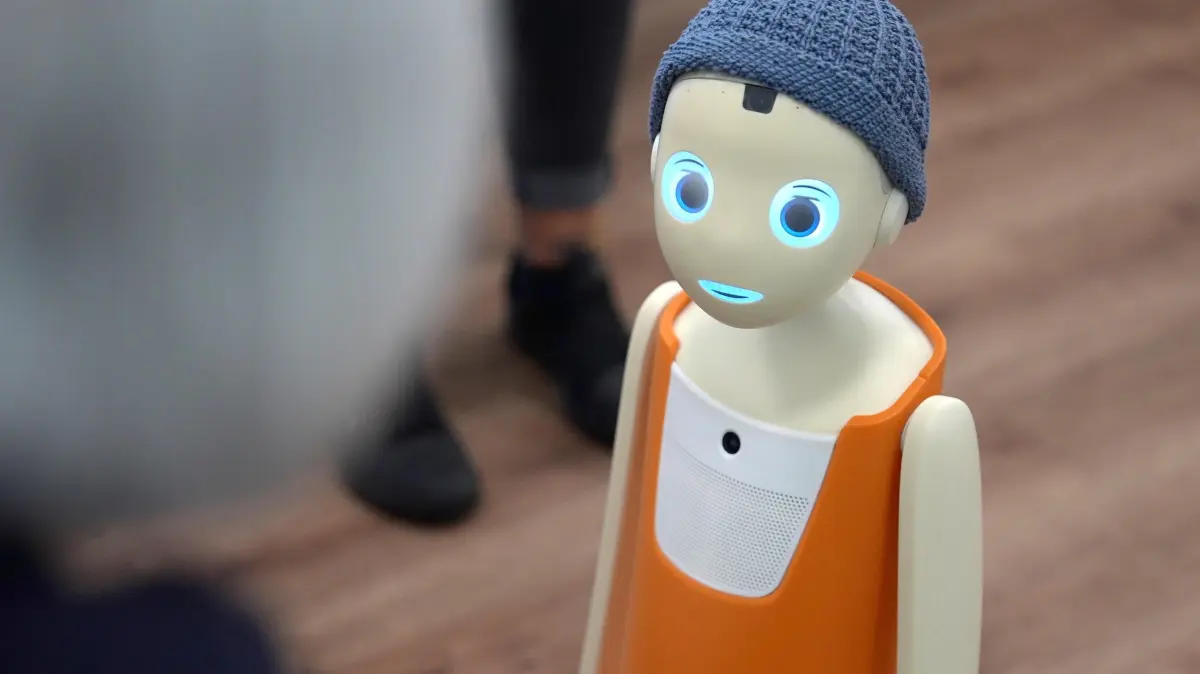 Einfach mal plaudern: Roboter Ricky im Seniorenheim: Roboter Ricky im Johanniter-Stift Hannover-Ricklingen (Foto vom 17.06.2025). Ricky ist ein sogenannter Empathie-Roboter, das heisst, er kann Stimmlage und Mimik seines Gegenuebers "lesen" und einfuehlsam reagieren. Er kann seinen Kopf bewegen, Blickkontakt aufbauen und erfuellt mit seinen Kulleraugen das Kindchenschema. Das Roboter-Modell heisst "Navel" und wurde von der Muenchner Firma Navel Robotics entwickelt. Es greift auf ChatGPT zurueck, laeuft ueber WLAN und kann sich Namen und Informationen merken. Den Angaben zufolge ist der Roboter datenschutzkonform. Informationen werden direkt auf ihm und nicht in der Cloud gespeichert. (Siehe epd-Feature und Video vom 10.07.2025)