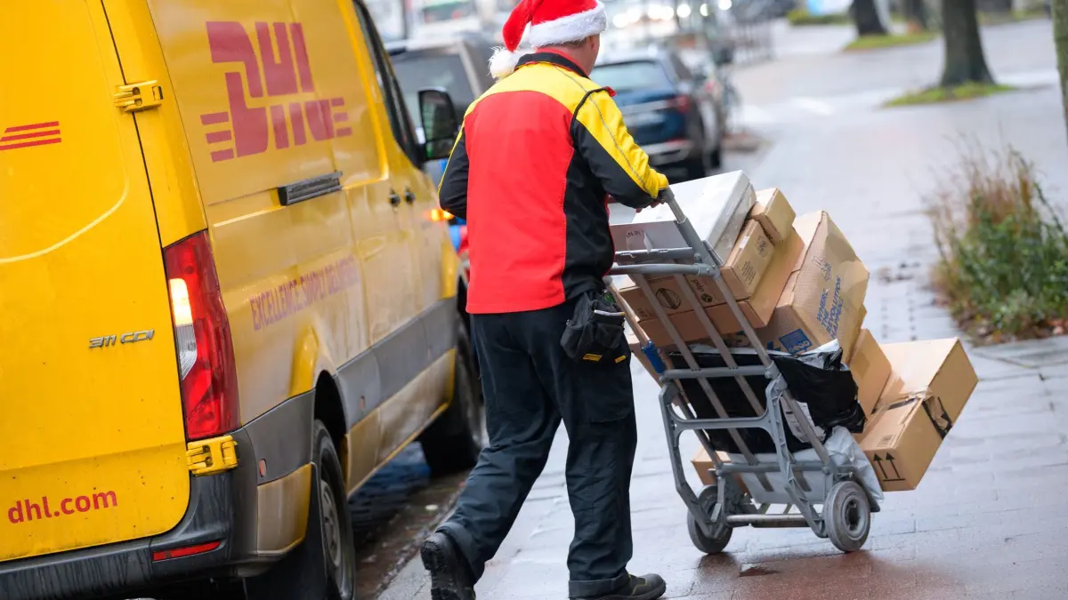 Online-Handel trägt zur Verschuldung bei: ARCHIV - 24.12.2021, Hamburg: Ein Paketbote des Paketdienstes DHL schiebt mit einer Weihnachtsmütze auf dem Kopf seine Fracht an seinem Transporter vorbei. (zu dpa: «Junge Leute häufiger im Online-Handel verschuldet») Foto: Jonas Walzberg/dpa +++ dpa-Bildfunk +++