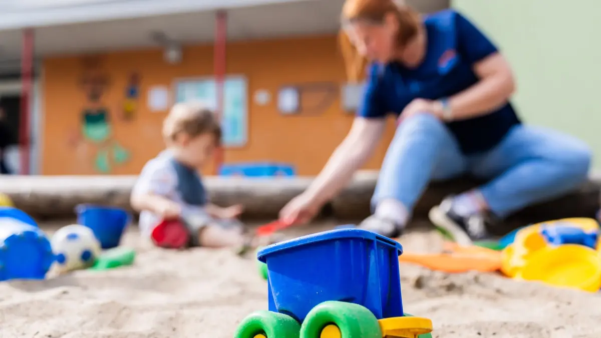 ARCHIV - 23.08.2024, Berlin: Ein Kind spielt mit einer Erzieherin im Sandkasten einer Kita. Die hochumstrittenen Lockerungen der Personalvorgaben in nordrhein-westfälischen Kitas können ab sofort umgesetzt werden. (zu dpa: «Umstrittene Kita-Personalverordnung in Kraft») Foto: Christoph Soeder/dpa +++ dpa-Bildfunk +++