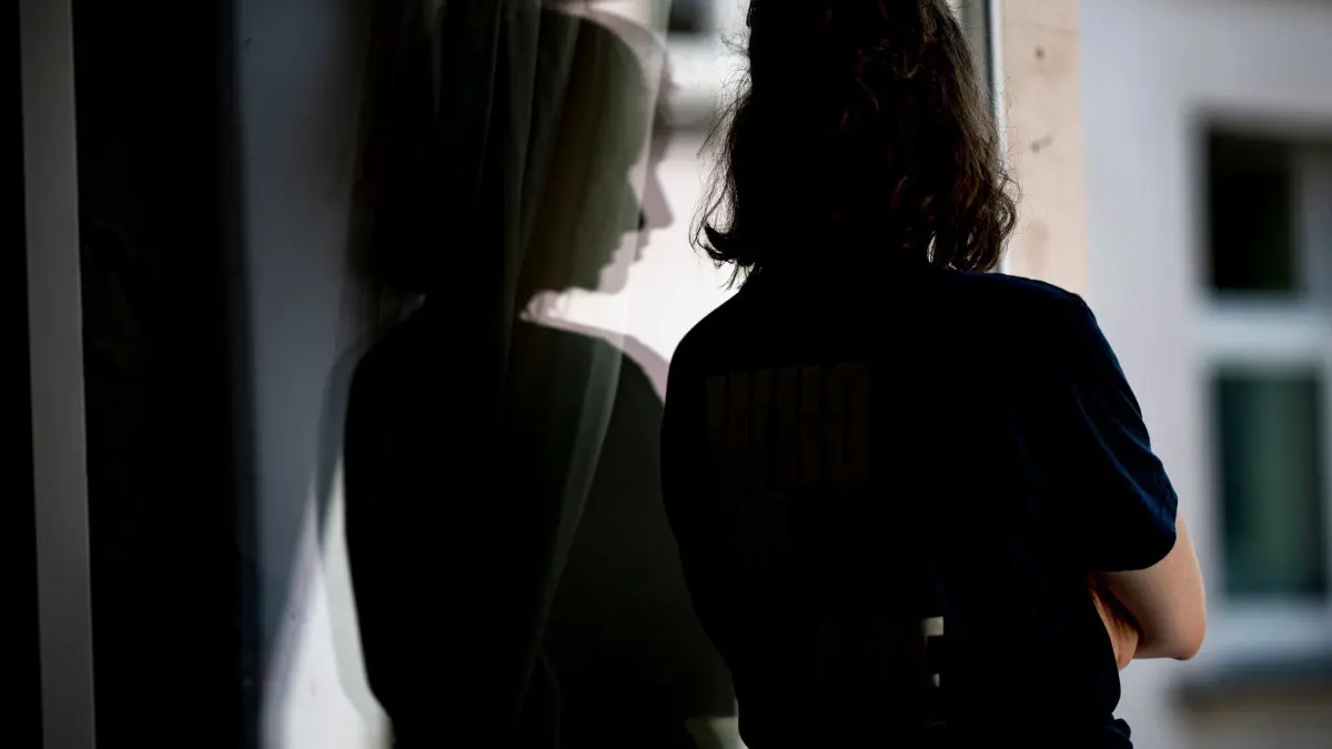Frau steht mit verschränkten Armen in ihrer Wohnung am Fenster: ILLUSTRATION - Eingestehen, dass etwas nicht stimmt: Je früher die Erkrankung erkannt wird, desto besser greifen Behandlungen. (zu dpa: «Hochfunktionale Depression: Wie man sie erkennt - was hilft») Foto: Fabian Sommer/dpa/dpa-tmn - Honorarfrei nur für Bezieher des dpa-Themendienstes +++ dpa-Themendienst +++