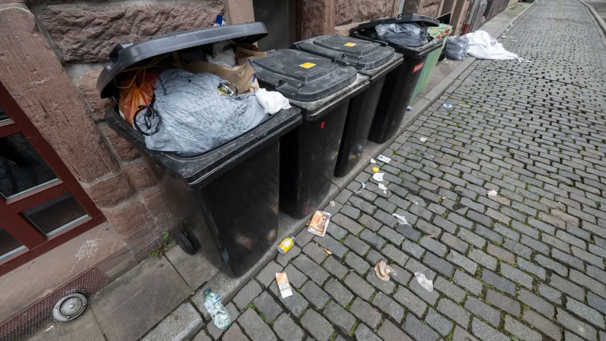 Überquellende Mülltonnen und Abfall in Gasse: ARCHIV - 20.05.2026, Baden-Württemberg, Stuttgart: Zahlreiche Mülltonnen stehen in einer Gasse des Leonhardsviertel in der Innenstadt vor einer mit Graffiti besprühten Hauswand neben Abfall, der verstreut auf dem Kopfsteinpflaster liegt. (zu dpa: «Städte kämpfen mit immer mehr Müll») Foto: Marijan Murat/dpa +++ dpa-Bildfunk +++