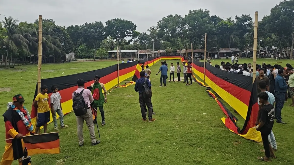 7,5 Kilometer lange deutsche Flagge genäht: PRODUKTION - 09.06.2026, Bangladesch, Nishchintapur: Fans haben sich an einer Seite versammelt, während die riesige, 7,5 Kilometer lange deutsche Flagge auf dem Schulplatz von Nishchintapur im bangladeschischen Distrikt Magura, knapp 200 Kilometer westlich der Hauptstadt Dhaka, entrollt wurde. Die riesige Fahne wurde von dem bangladeschischen Bauern Amjad Hossain als Zeichen der Dankbarkeit genäht, nachdem er vor mehr als zwei Jahrzehnten dank deutscher Medikamente von einer schweren Krankheit geheilt worden war. (zu dpa: «Fan aus Bangladesch näht 7,5-Kilometer-Fahne für DFB-Team») Foto: Nazrul Islam/Nerob Hossain/dpa +++ dpa-Bildfunk +++