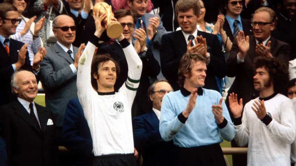 Manche Dinge kommen nicht wieder: Kapitän Franz Beckenbauer (2. v.li.) präsentiert am 7. Juli 1974 im Olympiastadion München stolz den FIFA Weltpokal mit Torwart Sepp Maier (Mi.) und Paul Breitner (re.). Bundespräsident Walter Scheel (li.) ist fast so stolz wie jetzt Kanzler Friedrich Merz nach dem Flop der deutschen Kicker gegen Paraguay am 29. Juni 2026 in Boston.