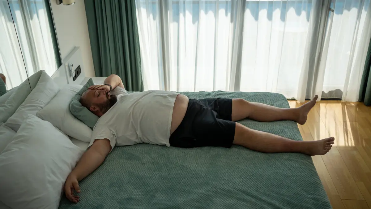 So bitte nicht! Fauler, erschöpfter, übergewichtiger Mann, der im Bett schläft und sich im Urlaub im Hotelzimmer schlecht fühlt.