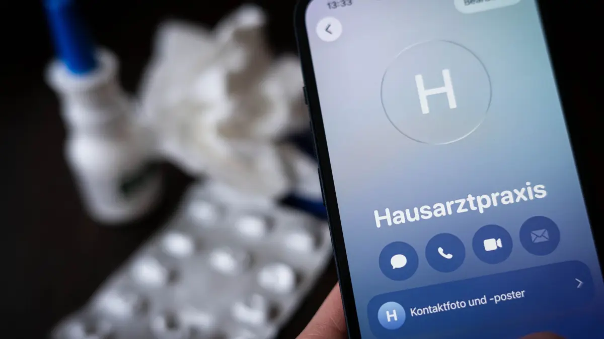 Krankschreibung per Telefon: ILLUSTRATION - 18.02.2026, Bremen: Eine Person hält ein Smartphone in der Hand und ruft eine Hausarztpraxis an. Im Hintergrund liegen ein Blister mit Tabletten, ein Nasenspray und ein Taschentuch auf einem Tisch. (zu dpa: «Erschwerte Krankmeldungen - vieles noch unklar») Foto: Sina Schuldt/dpa +++ dpa-Bildfunk +++