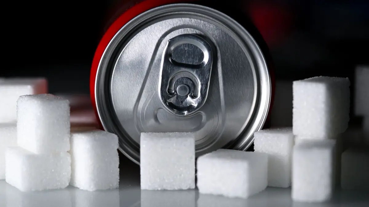 Softdrinks mit Zucker: ILLUSTRATION - 17.02.2026, Bayern, München: Eine Getränkedose mit einem Softdrink und zahlreiche Zuckerwürfel liegen auf einem Tisch. (zu dpa: «Mehr Schulden, weniger Finanzhilfen - das steckt im Haushalt») Foto: Sven Hoppe/dpa +++ dpa-Bildfunk +++