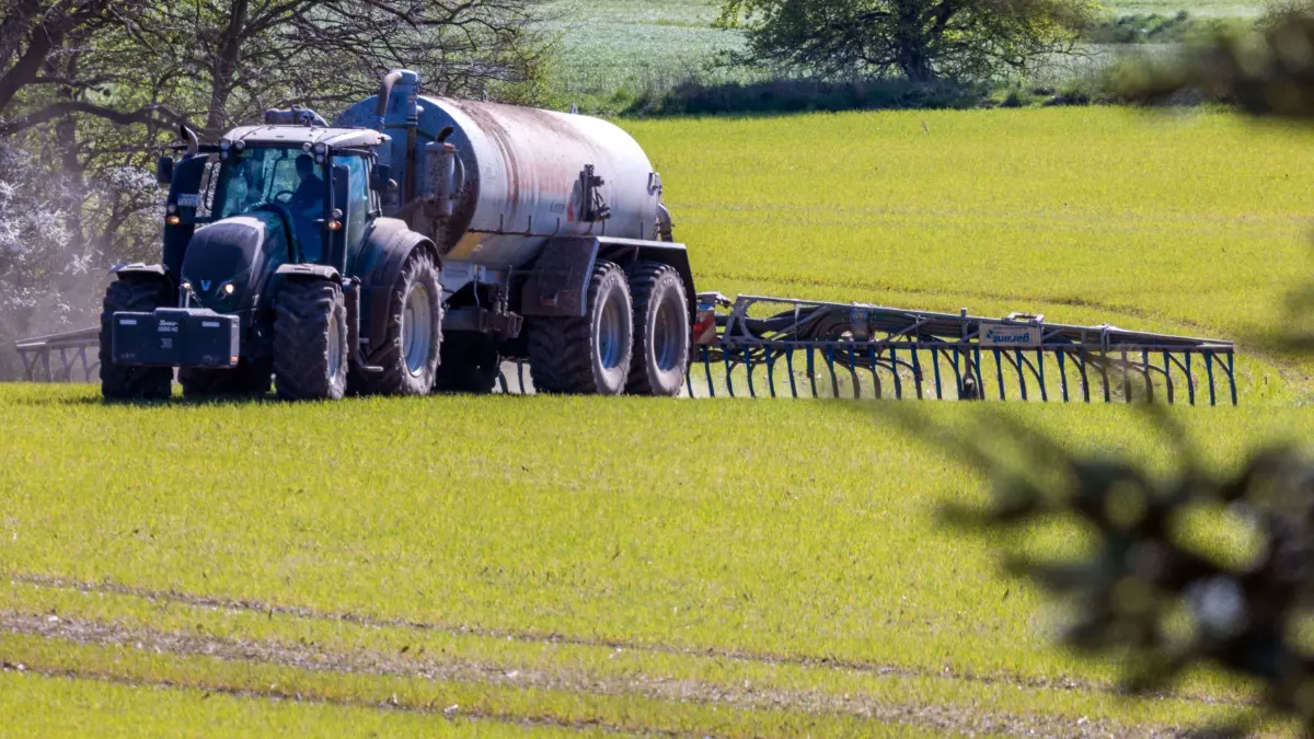 Ackerdüngung mit Gülle: ARCHIV - 26.04.2022, Mecklenburg-Vorpommern, Lützow: Ein Traktor zieht einen Tankwagen über ein Feld und verteilt Gülle im Boden. (zu dpa: «EU-Kommission: Milliarden-Kosten durch Stickstoffbelastung») Foto: Jens Büttner/dpa +++ dpa-Bildfunk +++