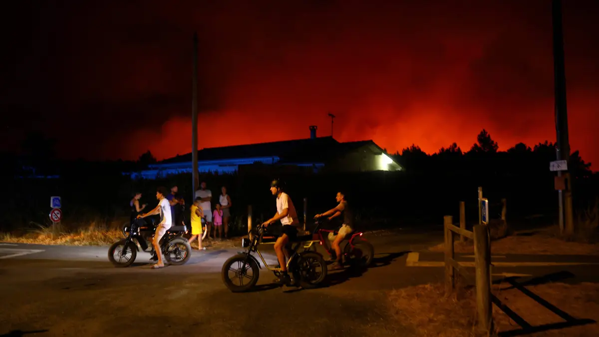 Le Porge: Jugendliche fahren während eines Waldbrands in Le Porge im Südwesten Frankreichs mit ihren Fahrrädern an einem brennenden Gebiet vorbei.