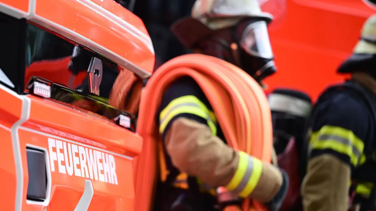Feuerwehr: PRODUKTION - 11.06.2026, Baden-Württemberg, Stuttgart: Zwei Feuerwehrleute gehen mit ihrer Ausrüstung zur Brandbekämpfung an einem Einsatzfahrzeug vorbei (gestellte Szene). (zu dpa: «Feuerwehr rettet 86-Jährige aus brennendem Haus») Foto: Bernd Weißbrod/dpa +++ dpa-Bildfunk +++