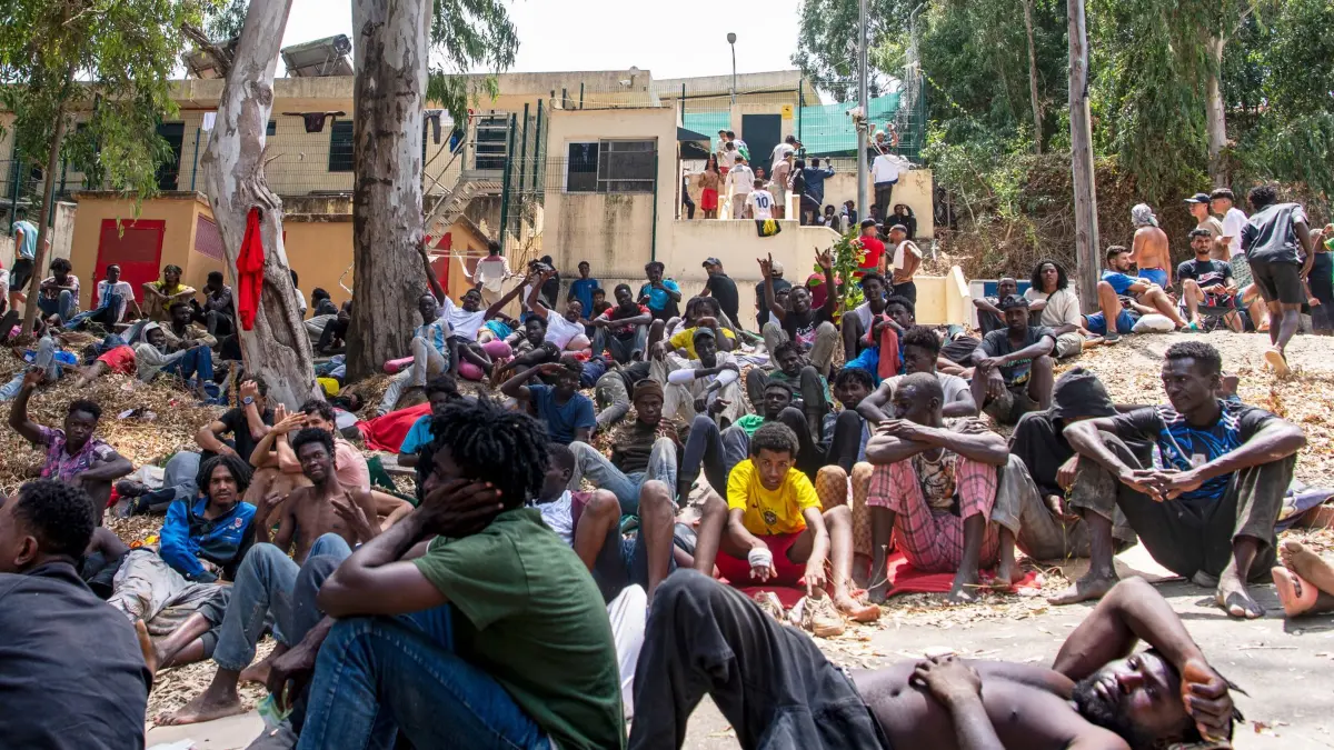 Migranten in Spanien - Ceuta: 31.07.2026, Spanien, Ceuta: Migranten ruhen sich vor einem Zentrum für die vorübergehende Aufnahme von Einwanderern (CETI) aus, nachdem sie von Marokko aus in die spanische Exklave Ceuta eingereist sind. Foto: Antonio Sempere/AP/dpa +++ dpa-Bildfunk +++
