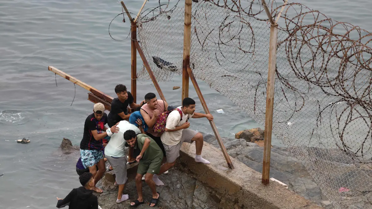 MOROCCO-SPAIN-MIGRATION: People gather along the fence at the site of clashes near Fnideq, on the Morocco-Spain border, on July 31, 2026. Thousands of migrants crossed overnight from Morocco into Spain's north Africa's Ceuta enclave, a police source said on July 31, adding that it was impossible to estimate how many people in total. A total of 18 people died while attempting to reach the Spanish enclave, the source said. (Photo by Abdel Majid BZIOUAT / AFP)