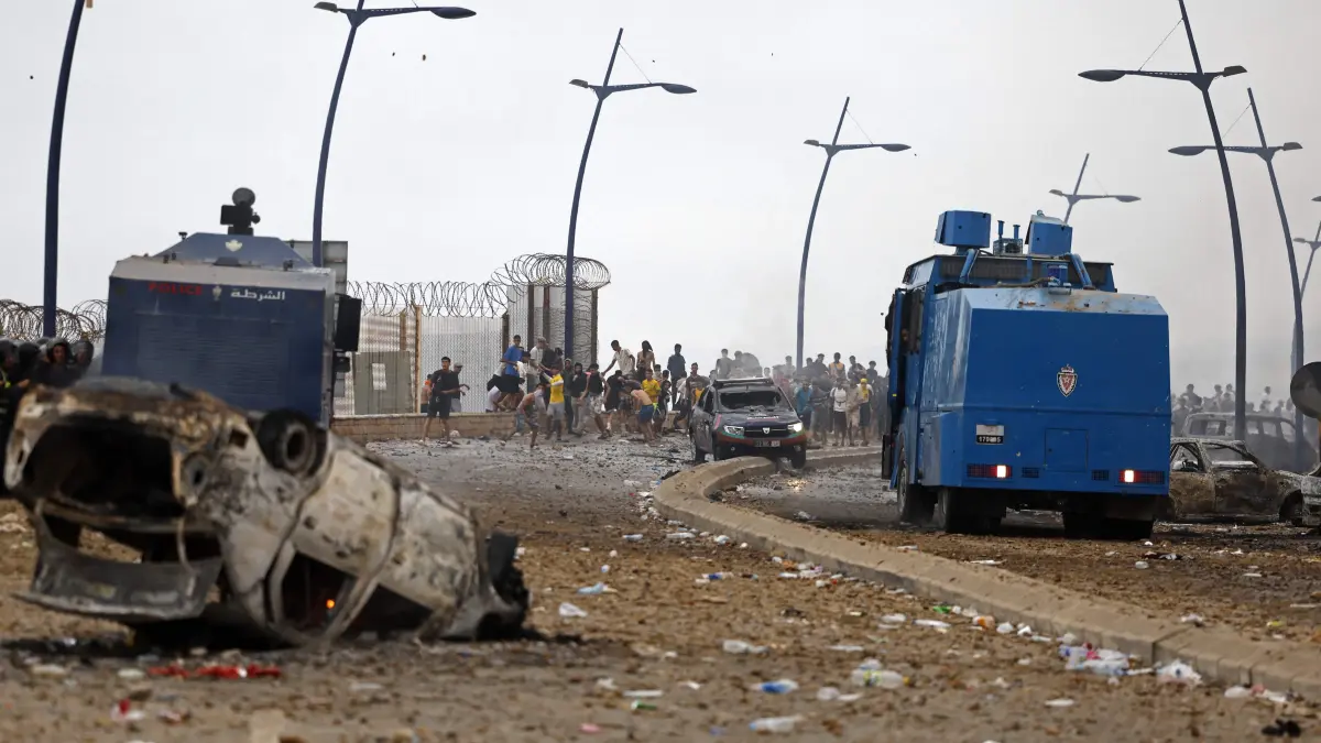 MOROCCO-SPAIN-MIGRATION: Members of Moroccan security forces (L) and people gather at the site of clashes near Fnideq, on the Morocco-Spain border, on July 31, 2026. Thousands of migrants crossed overnight from Morocco into Spain's north Africa's Ceuta enclave, a police source said on July 31, adding that it was impossible to estimate how many people in total. A total of 18 people died while attempting to reach the Spanish enclave, the source said. (Photo by Abdel Majid BZIOUAT / AFP)