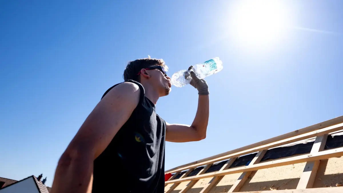 Arbeiten bei Hitze: ARCHIV - 26.05.2026, Nordrhein-Westfalen, Sankt Augustin: Ein Dachdecker trinkt Wasser unter der sengenden Sonne bei über 30 Grad auf dem Dach eines Hauses. (zu dpa: «Psychologin gefragt: Gewöhnen wir uns an die Hitze?») Foto: Benjamin Westhoff/dpa +++ dpa-Bildfunk +++