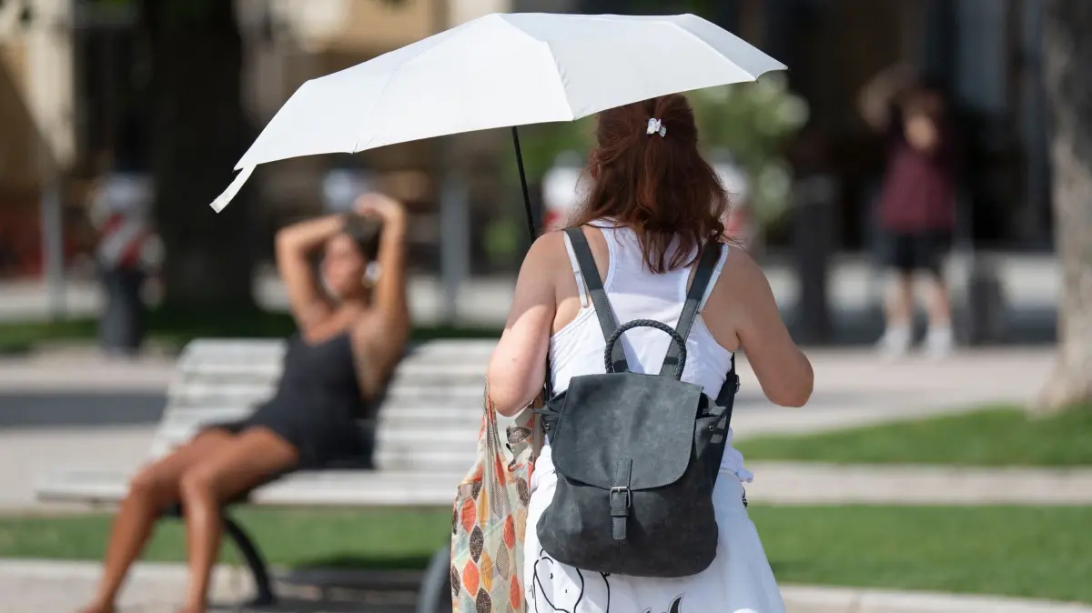 Sonne in Baden-Württemberg: 04.08.2026, Baden-Württemberg, Ludwigsburg: Eine Frau geht mit einem Sonnenschirm über den Schlossplatz. Foto: Marijan Murat/dpa +++ dpa-Bildfunk +++