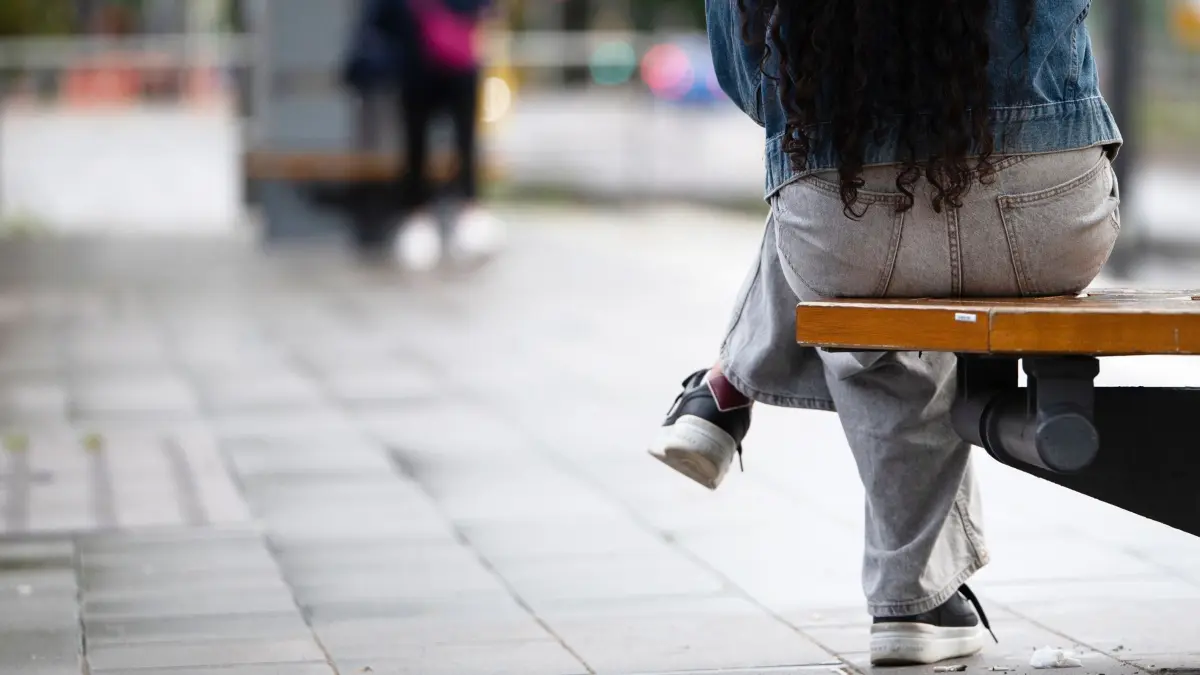 Eine junge Frau sitzt an einer Haltestelle auf einer Bank: ARCHIV - 01.08.2025, Baden-Württemberg, Stuttgart: Krisen verstärken Unsicherheiten oft noch - besonders in sensiblen Übergangsphasen, in denen sich junge Erwachsene oft befinden. (zu dpa: ««Faule Jugend»? Daten widersprechen dem Vorwurf») Foto: Markus Lenhardt/dpa/dpa-tmn +++ dpa-Bildfunk +++