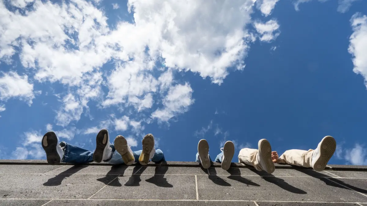 Wetter in Hessen: ARCHIV - 23.05.2021, Hessen, Bad Vilbel: Vier Jugendliche lassen auf einer hohen Mauer am Hafenpark ihre Beine vor dem locker bewölkten Himmel baumeln. (zu dpa: ««Faule Jugend»? Daten widersprechen dem Vorwurf») Foto: Frank Rumpenhorst/dpa +++ dpa-Bildfunk +++