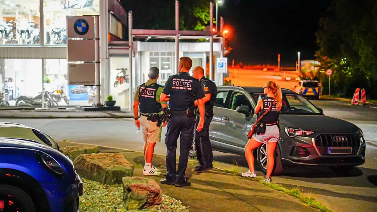 Person schießt auf PKW: 05.08.2026, Baden-Württemberg, Eningen unter Achalm: Einsatzkräfte der Polizei stehen am Tatort an einer Straße. Ein maskierter Täter war vor ein fahrendes Auto gesprungen und hatte auf den Wagen geschossen, der Fahrer wurde durch Splitter eines beschädigten Verkleidungsteils oberflächlich verletzt. Foto: Fotoreport-DB/dpa +++ dpa-Bildfunk +++