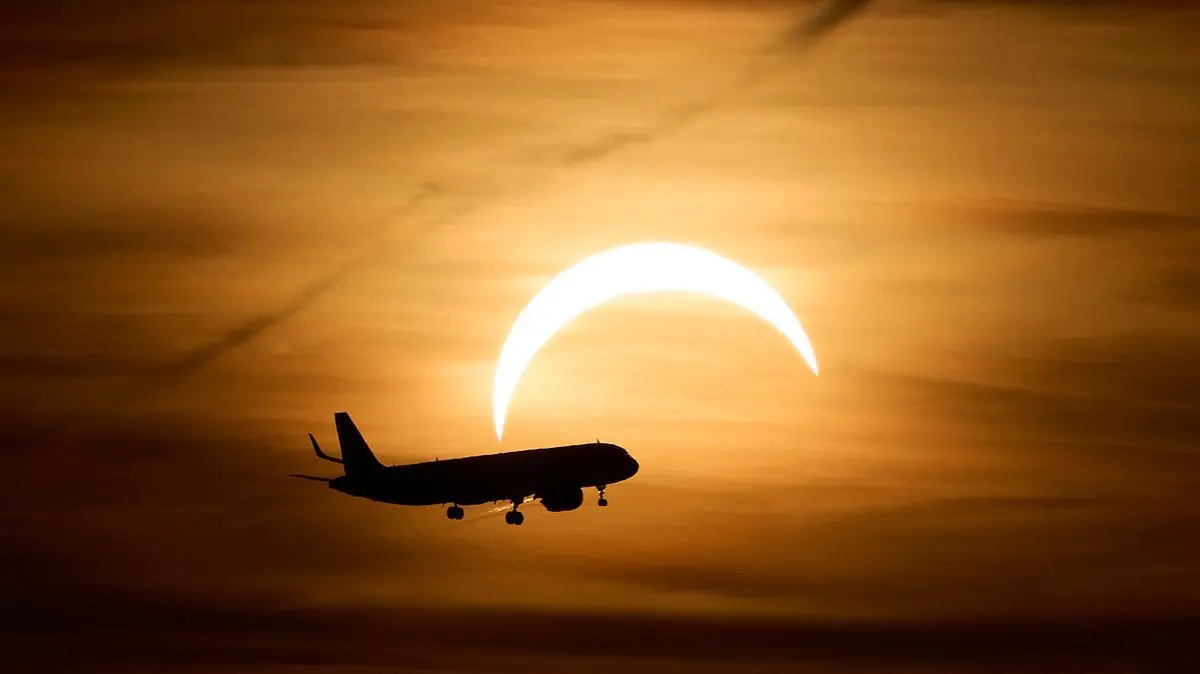 Ein Airbus A321 aus London fliegt während der partiellen Sonnenfinsternis im Landeanflug auf den Flughafen Berlin Brandenburg (BER) vor der teilweise vom Mond verdeckten Sonne.