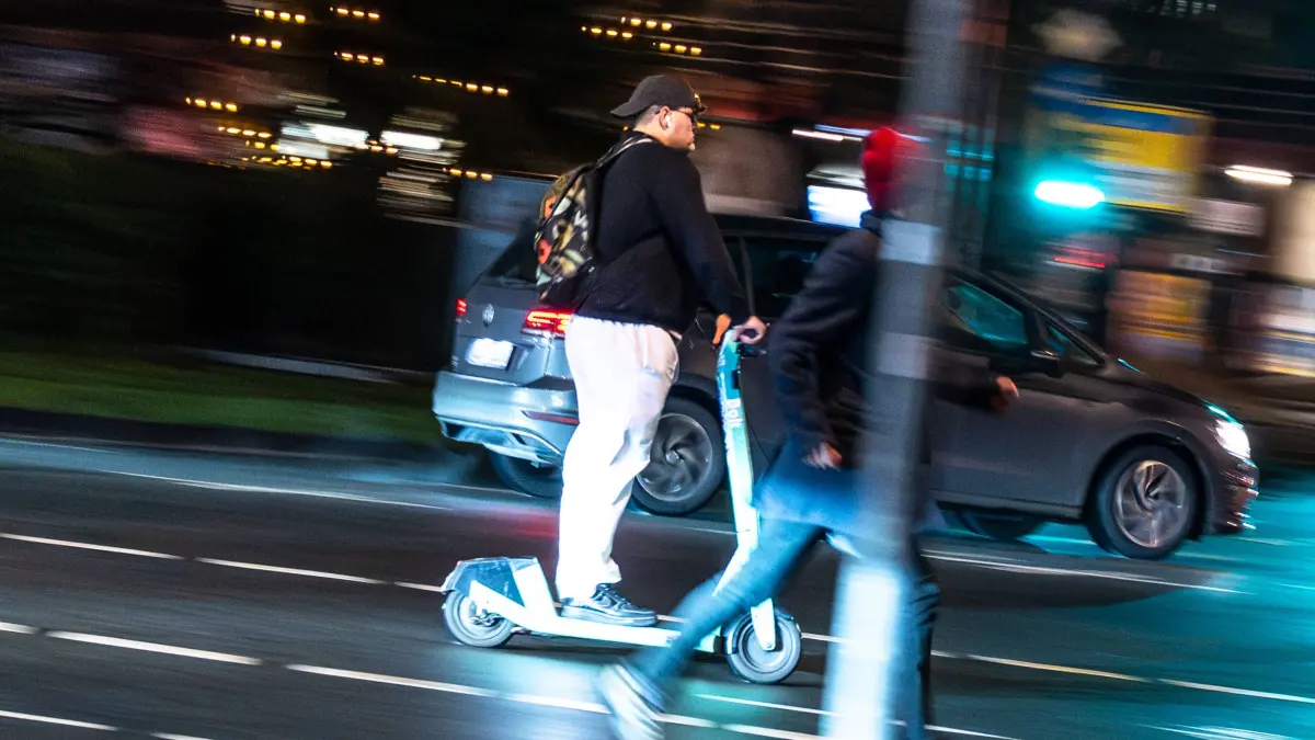 Verkehrsteilnehmer bei Nacht im Stadtverkehr Oldenburg, Deutschland, 09.12.2025: Ein E-Scooterfahrer fährt am Abend neben einem Fußgänger durch den nächtlichen Stadtverkehr. Leuchtende Ampeln, reflektierender Asphalt und vorbeifahrende Fahrzeuge prägen die Situation bei nasser Straße und winterlichen Lichtbedingungen. Dieses Motiv dient als Symbolbild für Themen rund um Verkehr, Sicherheit, Mobilität und die dunkle Jahreszeit. *** Road users at night in city traffic Oldenburg, Germany, 09 12 2025 An e-scooter rider rides next to a pedestrian through city traffic at night Glowing traffic lights, reflective asphalt and passing vehicles characterize the situation in wet road and winter light conditions This motif serves as a symbolic i