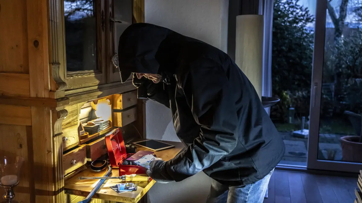 Symbolbild Wohnungseinbruch, Täter ist von der Gartenseite her, in eine Wohnung eingedrungen und sucht nach Beute, bricht eine Geldkassette auf, findet Wertgegenstände, Geld, Einbrecher *** Symbolic image of burglary, perpetrator has broken into an apartment from the garden side and is looking for loot, breaks open a cash box, finds valuables, money, burglar