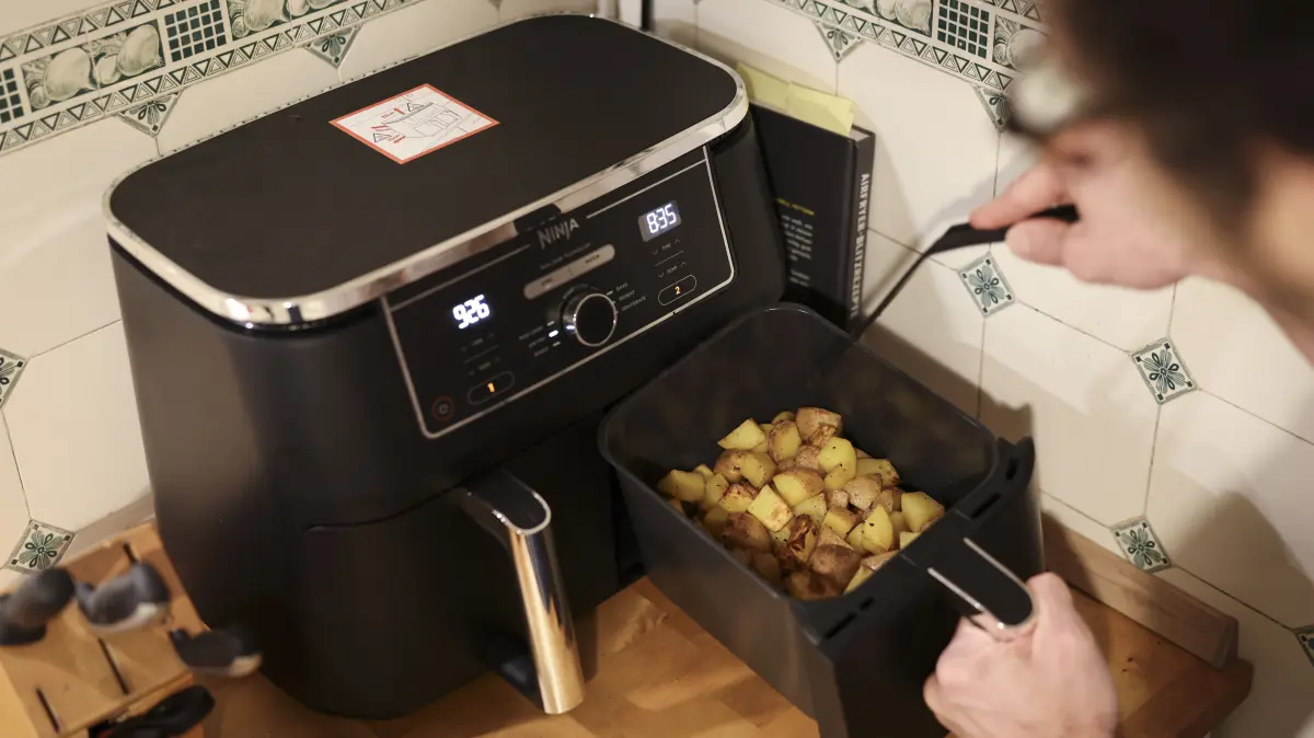 Ein Mann kocht in seiner Küchen mit einer Heißluftfritteuse (Airfryer) ein Gericht aus Kartoffelstücken und gebratenem Hühnerfleisch. (Symbolbild)