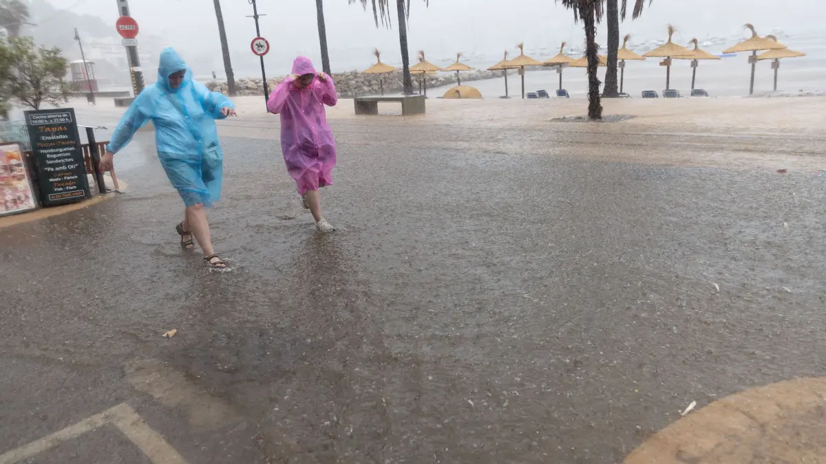 Wetter auf Mallorca: 09.09.2026, Spanien, Soller: Menschen gehen im Regen am Port de Sóller. Starke Regenfälle und heftige Winde sorgen für einen plötzlichen Temperatursturz auf der Insel. (zu dpa: «Frau ertrinkt bei Unwetter auf Mallorca») Foto: Clara Margais/dpa +++ dpa-Bildfunk +++