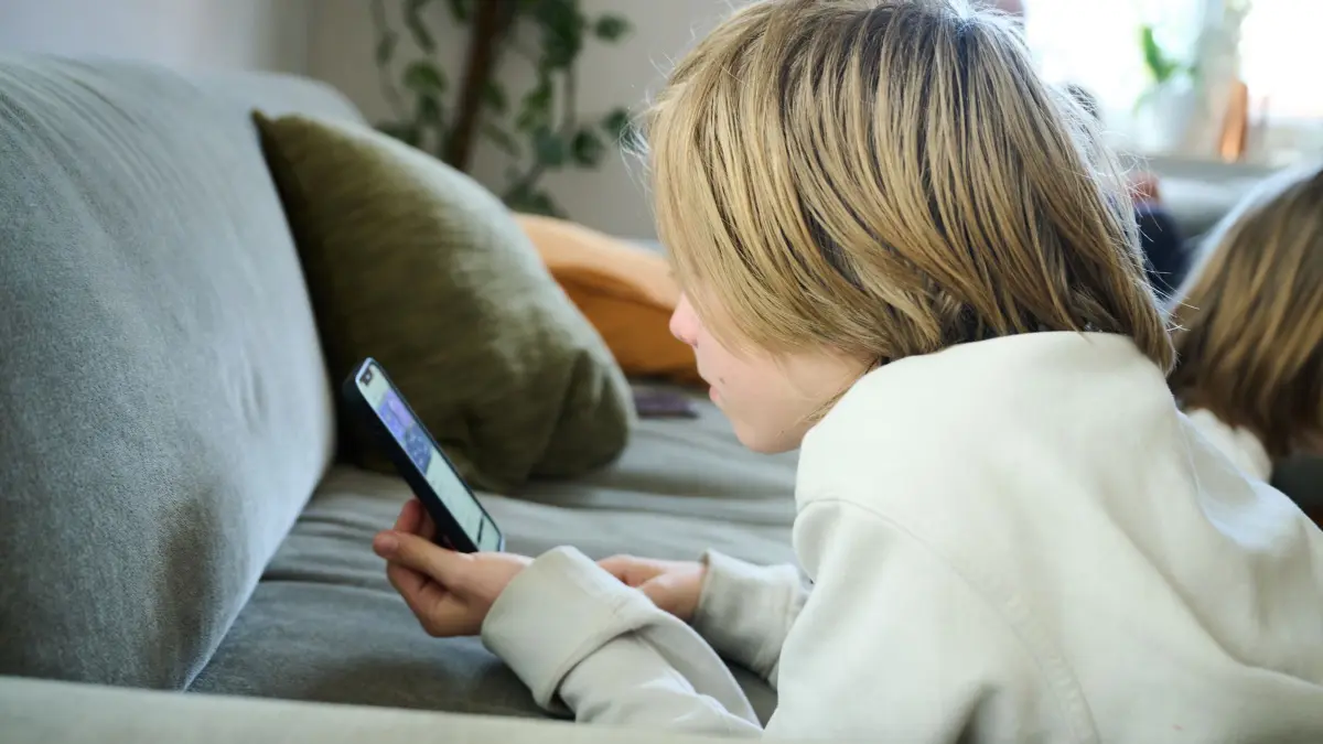 Symbolbild - Smartphone-Nutzung bei Kindern: ARCHIV - 21.04.2025, Bayern, Roth: ILLUSTRATION - Ein Junge liegt auf einem Sofa und guckt auf sein Smartphone. (gestellte Szene). (zu dpa: «Kommt ein Social-Media-Verbot für Kinder? Antworten erwartet») Foto: Annette Riedl/dpa +++ dpa-Bildfunk +++