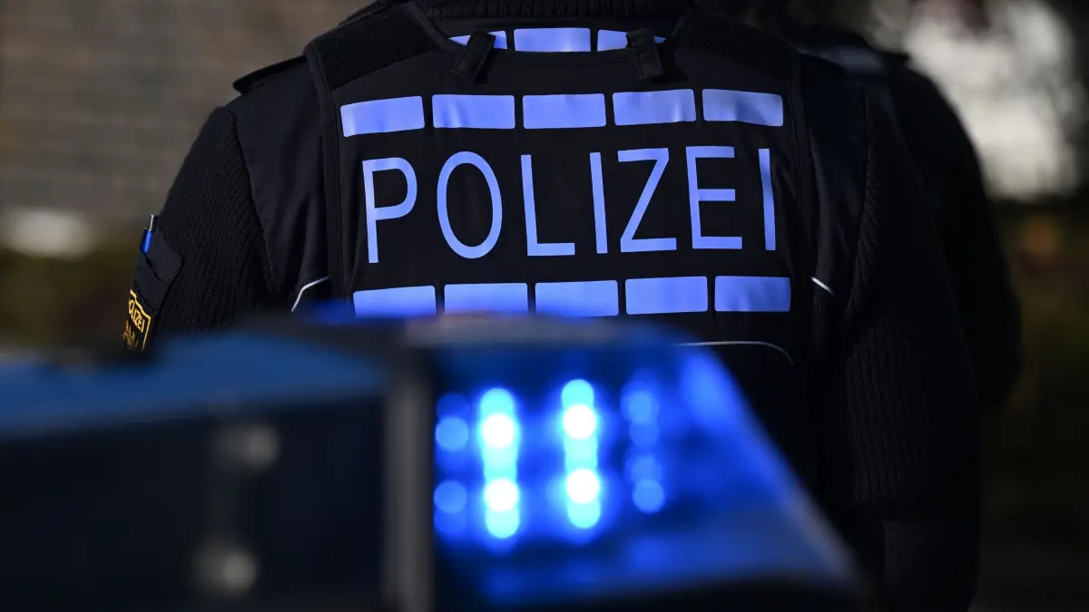 Polizei: Das Logo der Polizei auf der Dienstkleidung eines Polizisten der vor einem Blaulicht steht (gestellte Szene). (zu dpa: «Großeinsatz am Bundesgerichtshof – Mann klettert über Zaun»)