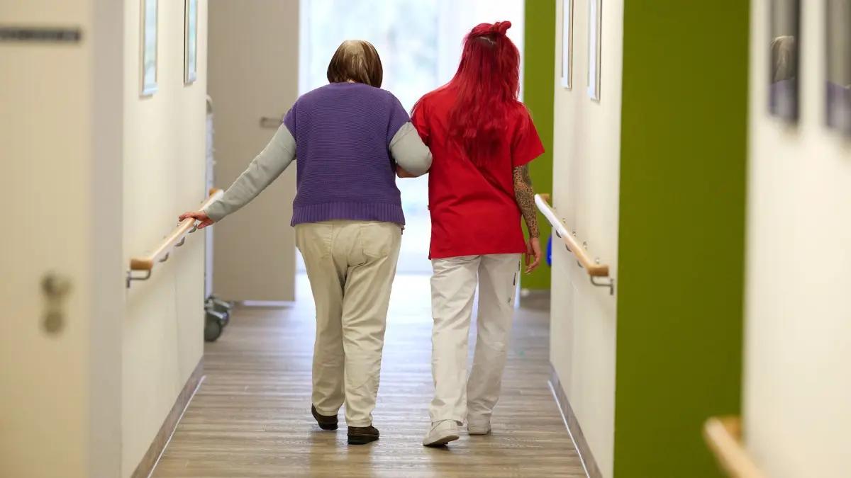 Pflegelöhne steigen - weiter Debatte über Reform: ARCHIV - 12.03.2025, Nordrhein-Westfalen, Essen: Eine Pflegekraft begleitet im DRK-Pflegezentrum Solferino eine Seniorin durch den Flur. (zu dpa: «Pflegekommission soll bis Anfang 2027 Reform vorschlagen») Foto: Bernd Thissen/dpa +++ dpa-Bildfunk +++