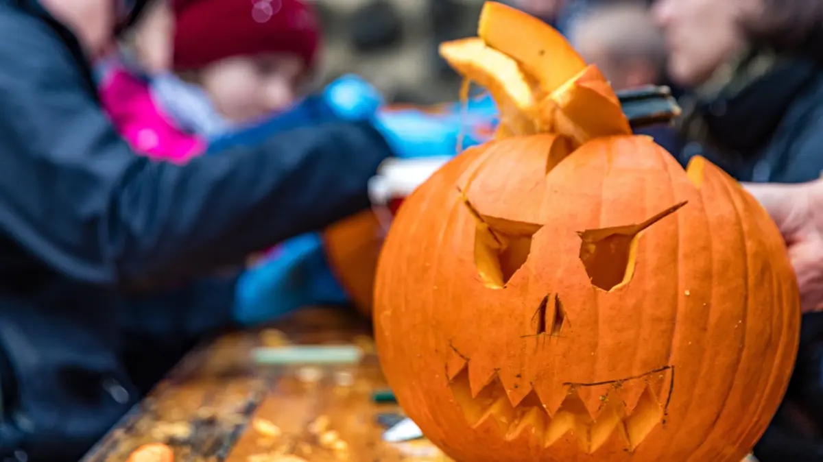 Halloween in der Slawenburg: Kinder sitzen mit ihren Eltern beim Halloween-Fest in der Slawenburg beim Kürbis-Schnitzen. (zu dpa: «Von Gruselhaus bis Drachenfest: Tipps für die Herbstferien»)
