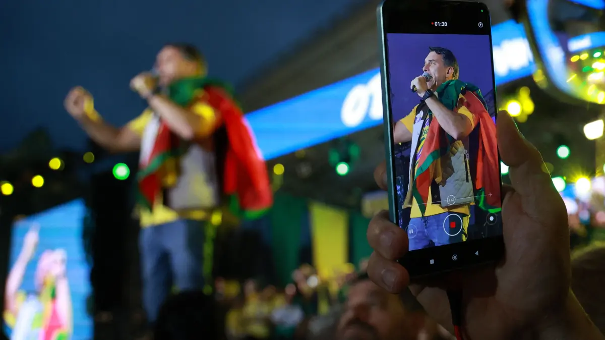 BRAZIL-ELECTION-RUNOFF-CAMPAIGN: A smartphone displaying Brazil's right-wing senator and Liberal Party (PL) presidential candidate Flavio Bolsonaro delivering a speech during a rally at Largo Glenio Peres in Porto Alegre, Brazil, on October 14, 2026, ahead of the presidential election runoff. Bolsonaro heads to a runoff election with leftist President Luiz Inacio Lula da Silva on October 25, buoyed by sweeping gains in Congress, after a shock first-place finish. (Photo by SILVIO AVILA / AFP)