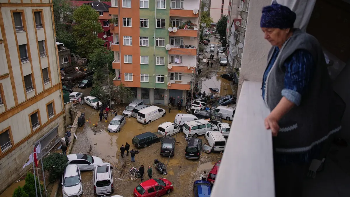 Unwetter in der Türkei: Eine Frau schaut von ihrem Balkon auf Anwohner, die zwischen umgestürzten Fahrzeugen und verstreuten Trümmern umher gehen, nachdem heftige Regenfälle zu Überschwemmungen geführt haben. (zu dpa: «Istanbul: Meteorologe warnt vor weiteren Überschwemmungen»)