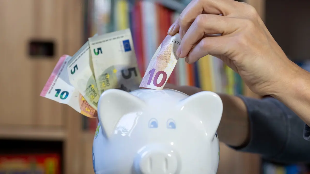 Sparen: ILLUSTRATION - Eine Frau steckt einen 10-Euro-Schein in ein Sparschwein. (zu dpa: «Schon als Kind fürs Alter vorsorgen - die Frühstartrente»)