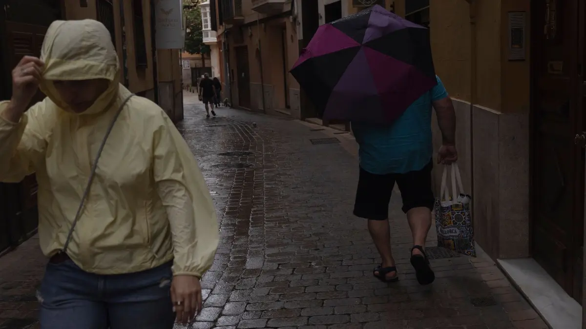Wetter auf Mallorca: Menschen gehen im Regen durch die Innenstadt von Palma. Der Sturm „Adam“ zieht gerade über die Insel hinweg, und für die Bevölkerung wurde eine rote Warnstufe ausgerufen. (zu dpa: «dpa-Morgenlage - 19. Oktober 2026»)