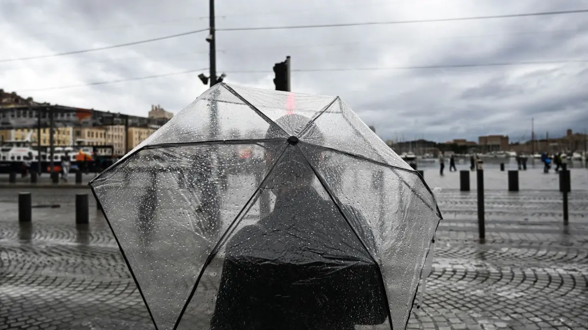 Unwetter in Frankreich: 20.10.2026, Frankreich, Marseille: Ein Fußgänger steht mit einem Regenschirm im Vieux Port (alter Hafen) in der südfranzösischen Mwetropole. Starke Regenfälle, die am 19. Oktober 2026 einsetzten, führten über Nacht zu erheblichen Überschwemmungen in mehreren Fließgewässern, vom Département Hérault bis zum Département Bouches-du-Rhône im Südosten Frankreichs, wodurch Dutzende Menschen evakuiert oder in Sicherheit gebracht werden mussten. Foto: Justine Meddah/AFP/dpa +++ dpa-Bildfunk +++