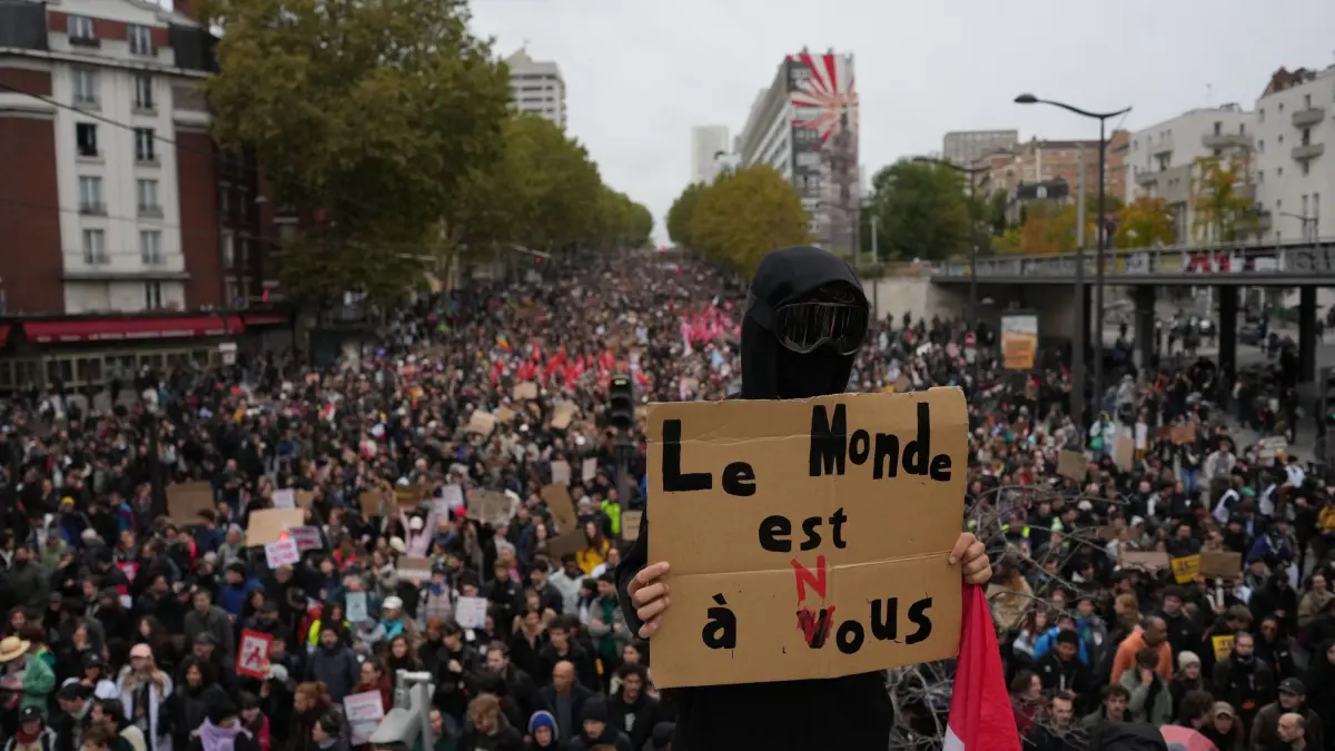 Proteste in Paris: Ein Demonstrant hält während einer Demonstration gegen steigende Lebenshaltungskosten in Paris ein Schild mit der Aufschrift „Die Welt gehört uns“ hoch. (zu dpa: «Mindestens 1.000 Festnahmen nach Protesten in Frankreich»)