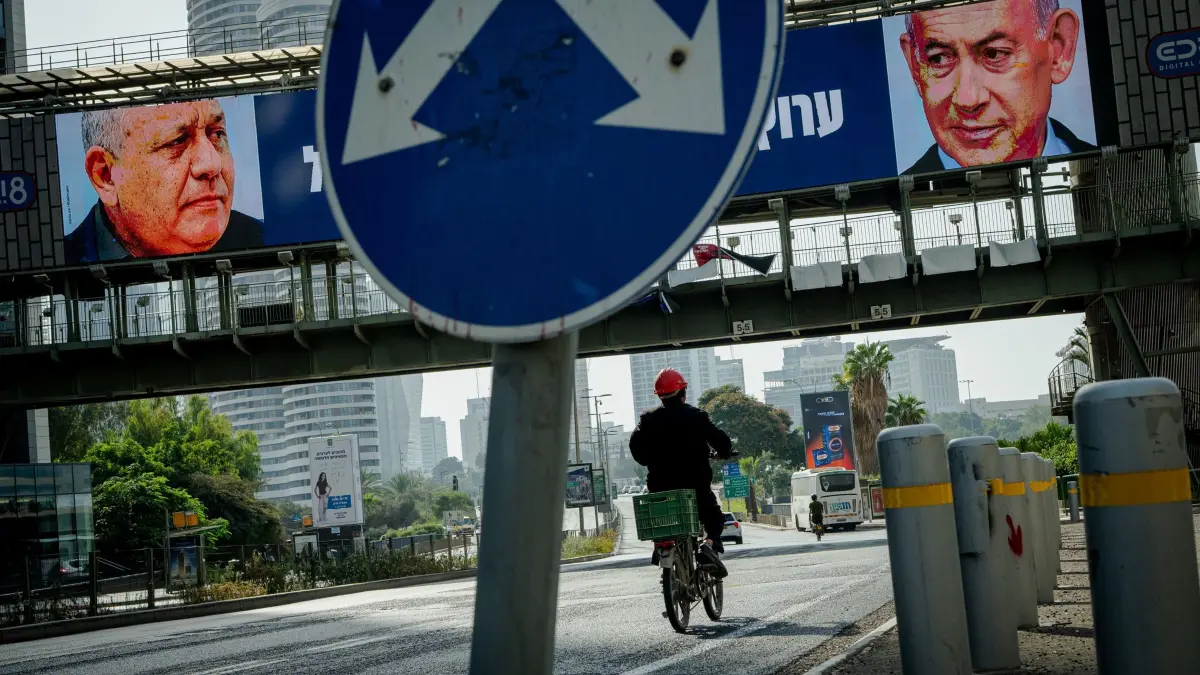 Nach der Parlamentswahl in Israel: Ein Radfahrer fährt unter einer Fußgängerbrücke hindurch, an der elektronische Wahlplakate zu sehen sind, auf denen der ehemalige Stabschef der israelischen Streitkräfte, Eisenkot (l), und Ministerpräsident Netanjahu (r) abgebildet sind. Am 27. Oktober finden in Israel Parlamentswahlen statt. (zu dpa: «Israels Wahl wird zur Zitterpartie – wie geht es nun weiter?»)